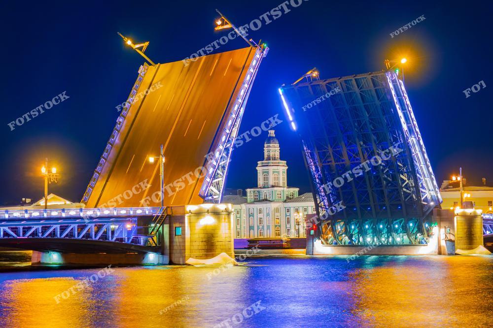 Фотография захватывает момент разведения Дворцового моста — одного из самых известных символов Санкт-Петербурга. На заднем плане виднеется здание Кунсткамеры, первого музея России, основанного Петром Великим. Ночная подсветка моста и его конструкций создает неповторимую атмосферу, подчеркивая величие архитектуры.